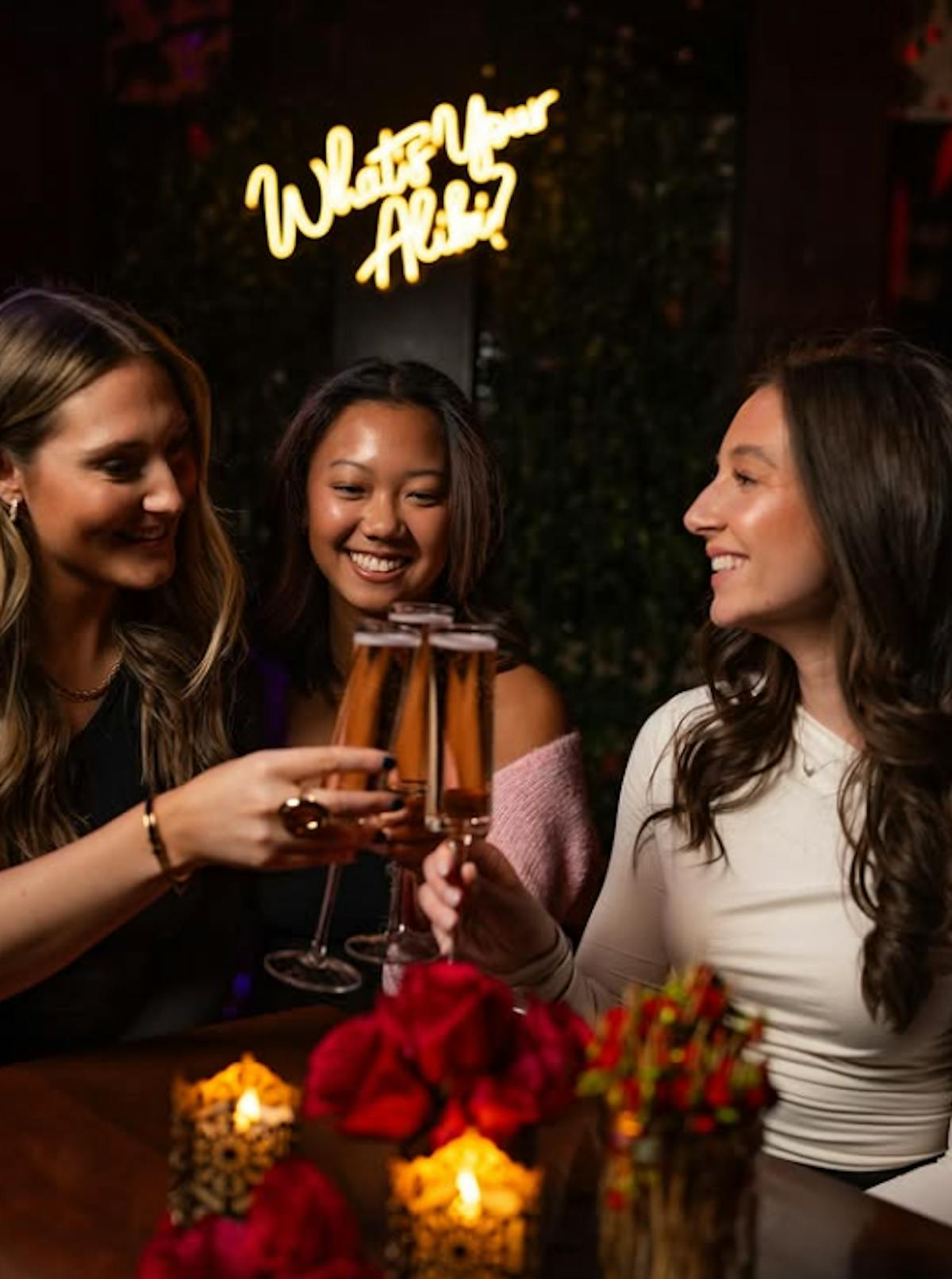 Friends toasting espresso martinis under the What’s Your Alibi neon
